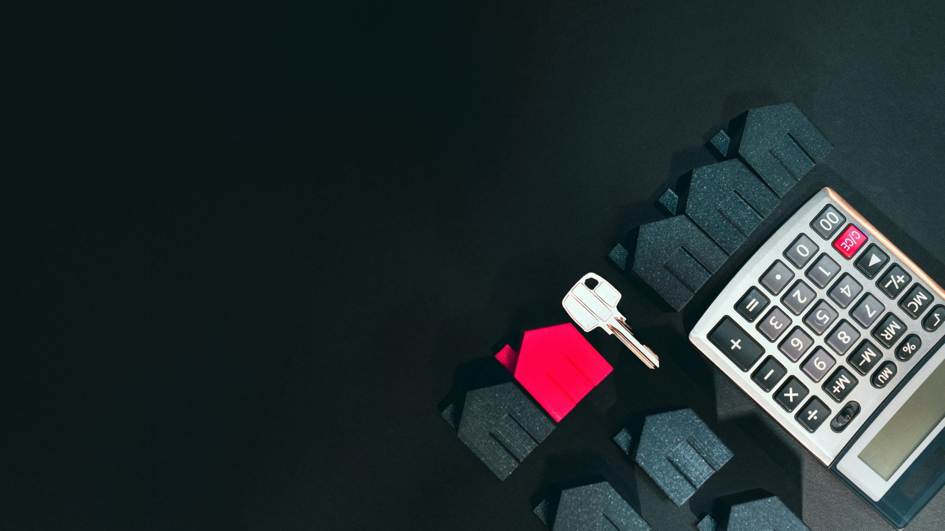 Immobilienkonzeptbild mit einem Taschenrechner, Häusern und einem Schlüssel auf schwarzem Hintergrund.